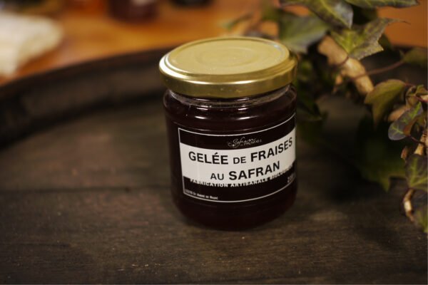 Présentation d'un pot de gelée de fraises au safran, sur le dessus d'un tonneau où un branche de lierre termine le décor