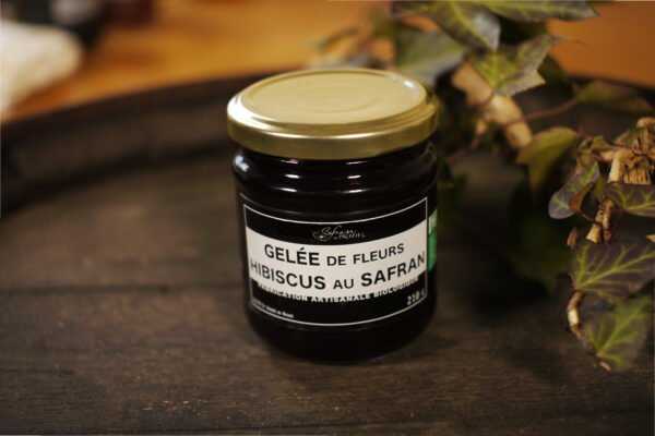 Présentation d'un pot de gelée de fleurs d'Hibiscus au safran, sur le dessus d'un tonneau où un branche de lierre termine le décor