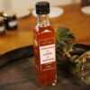 Présentation d'une bouteille de vinaigre de cidre au safran, sur le dessus d'un tonneau où un branche de lierre termine le décor. Logo de Safran du Pradel. En dessous, Fabrication artisanale biologique. 250ml