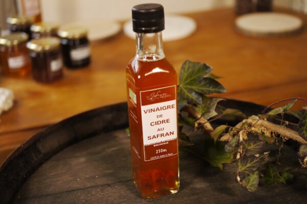 Présentation d'une bouteille de vinaigre de cidre au safran, sur le dessus d'un tonneau où un branche de lierre termine le décor. Logo de Safran du Pradel. En dessous, Fabrication artisanale biologique. 250ml