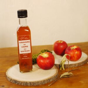 Sur deux planches rondes en bois, prennent place une bouteille de vinaigre de cidre au safran, trois pommes, des chatons de noisetier et un peu de mousse en arrière plan.