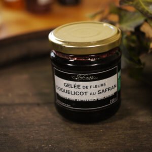 Présentation d'un pot de gelée de fleurs de coquelicot au safran, sur le dessus d'un tonneau où un branche de lierre termine le décor