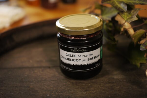 Présentation d'un pot de gelée de fleurs de coquelicot au safran, sur le dessus d'un tonneau où un branche de lierre termine le décor
