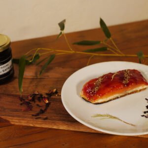 Sur une assiette posée sur une planche de présentation, un pavé de saumon recouvert degelée de fleurs d'Hibiscus au safran prêt à être dégusté. En arrière plan à gauche, un pot de gelée de fleurs d'Hibiscus au safran
